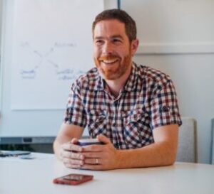 Arch GP sitting at a table in a meeting room, smiling