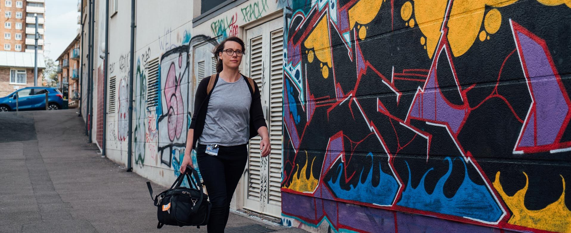 Arch nurse walking past graffitied wall, holding medical bag
