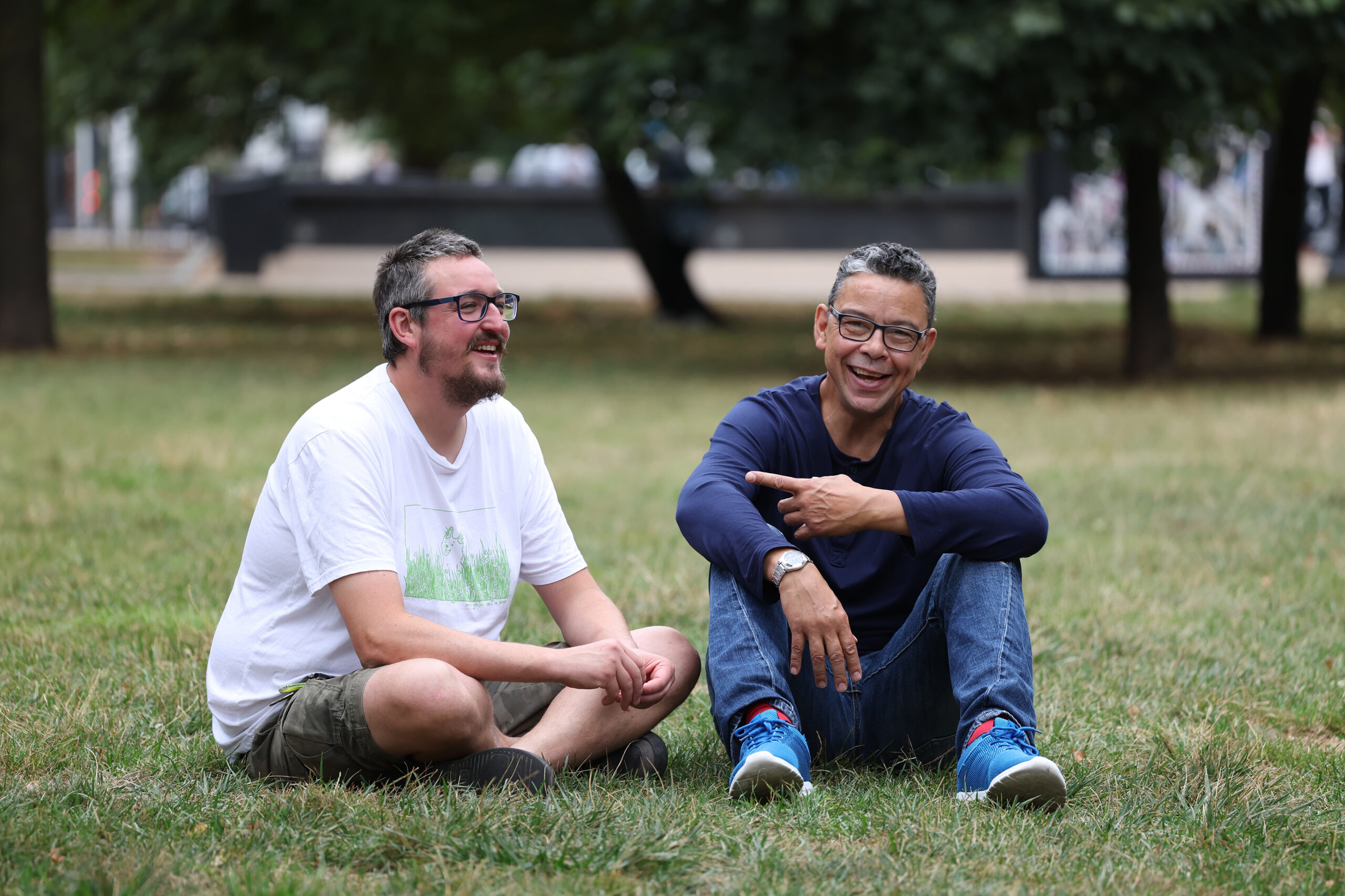 A health engagement worker and his client sit in the park laughing