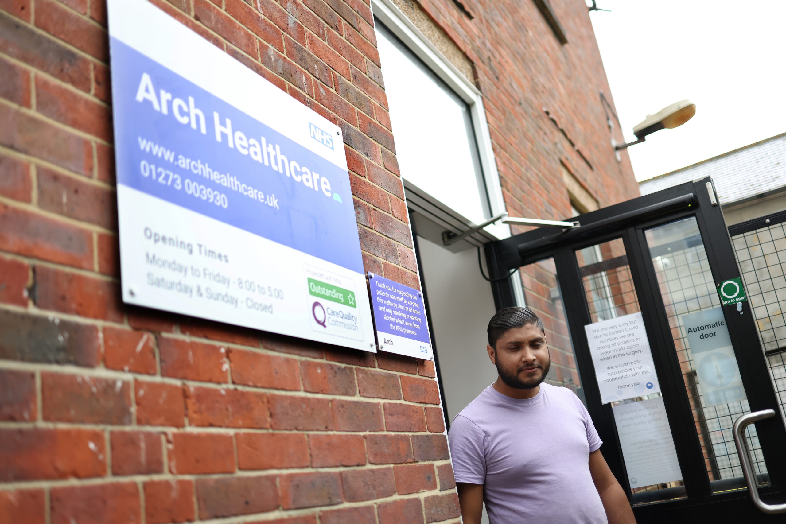 A patient walking out the front door of the Arch Healthcare surgery, with the front sign in clear visibility