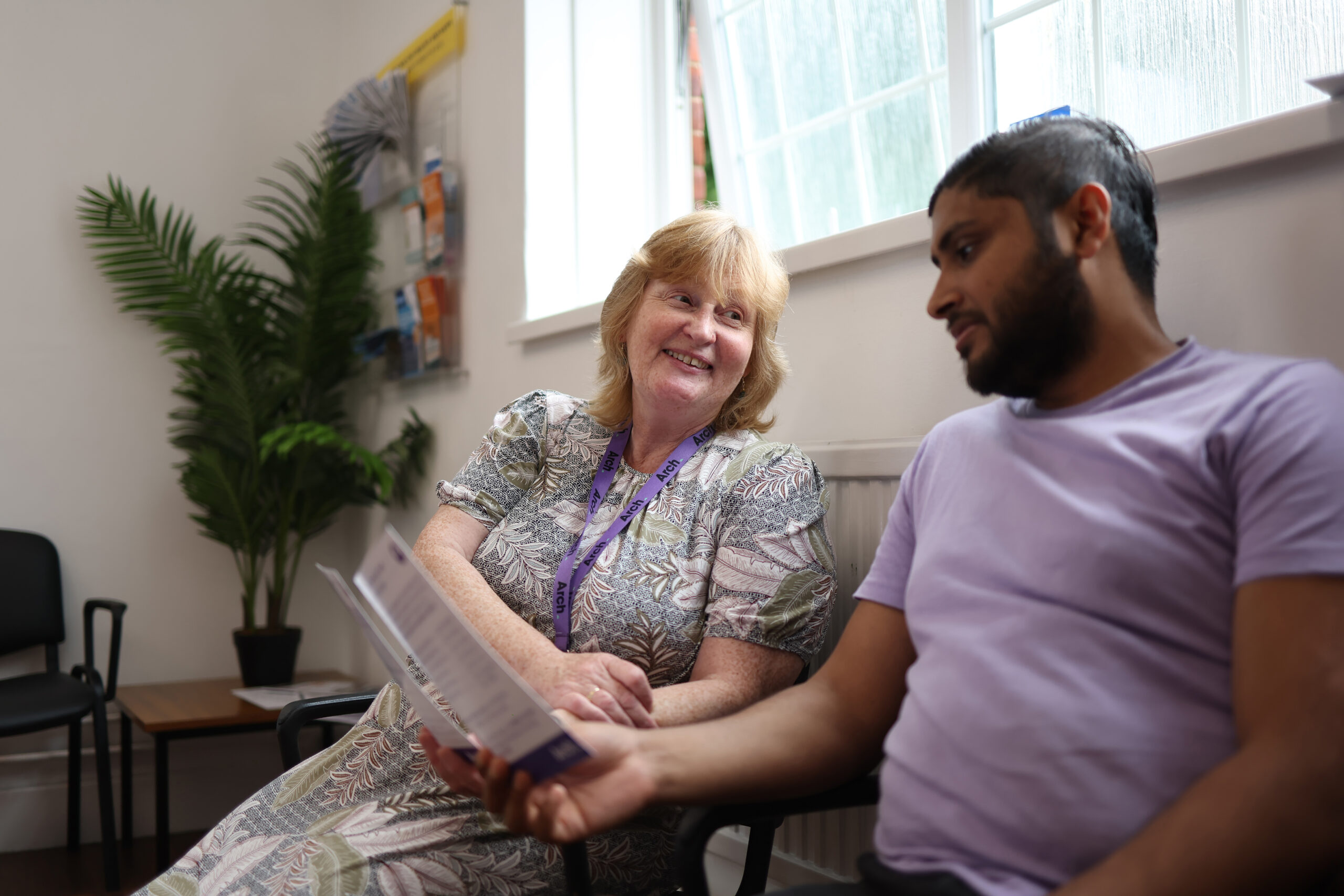 Patient and receptionist sitting together in the waiting room talking through a leaflet together, looking at leaflet and smiling