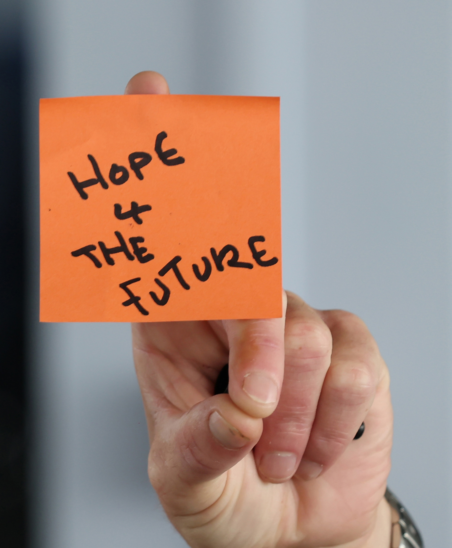 close up shot of someone's hand holding up orange post-it note with handwriting on, saying Hope for the Future