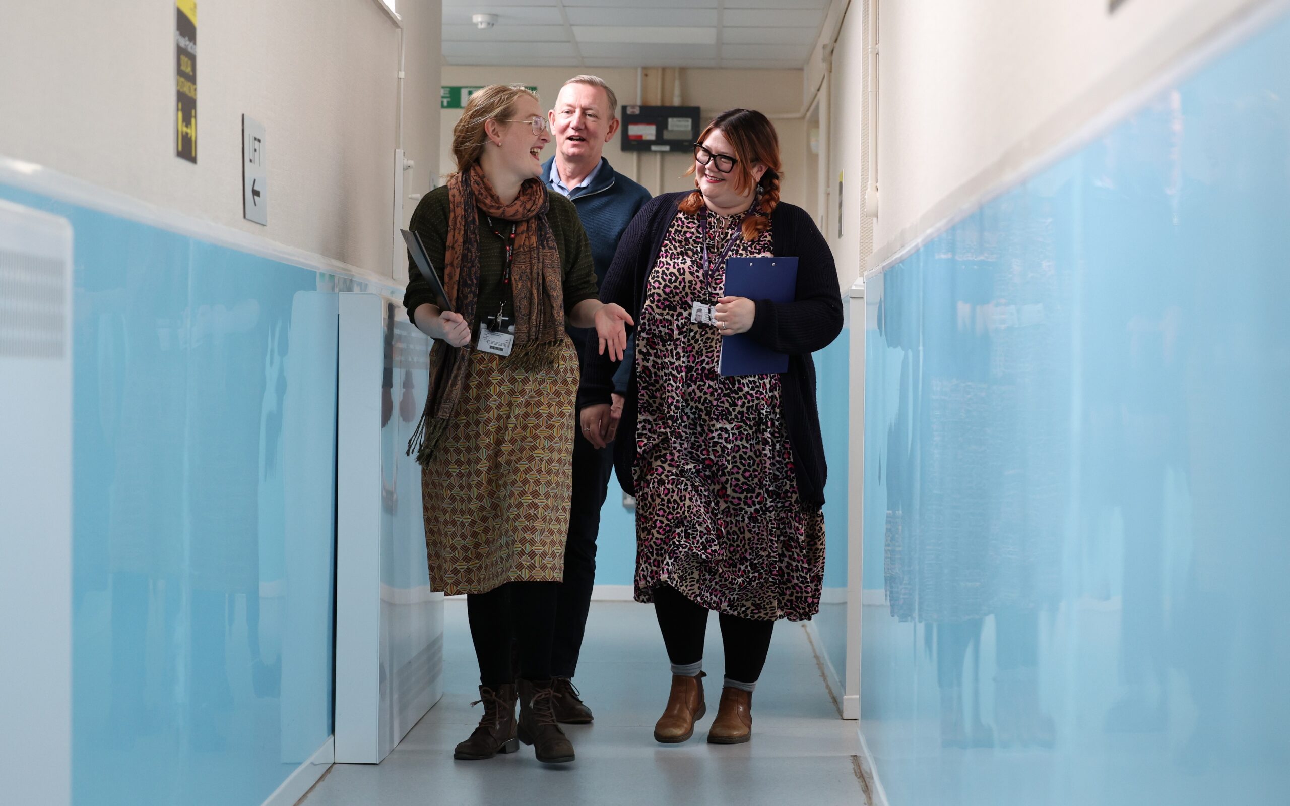 3 members of Arch's hospital inreach team, talking and chatting while they walk down a corridor, holding clipboards.