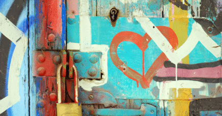 Close up of a wooden door, with colourful graffiti, including a red heart scribbled over a turquoise background.