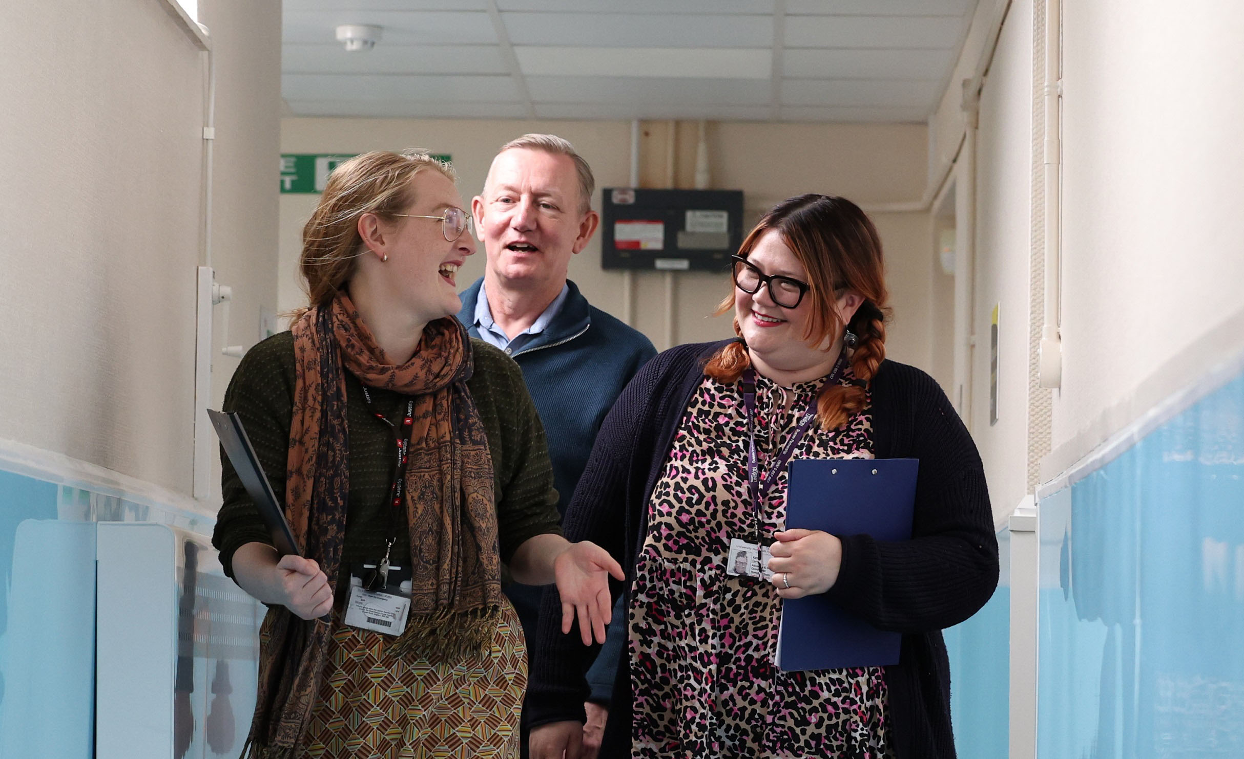 3 members of Arch's hospital inreach team, talking and chatting while they walk down a corridor, holding clipboards.