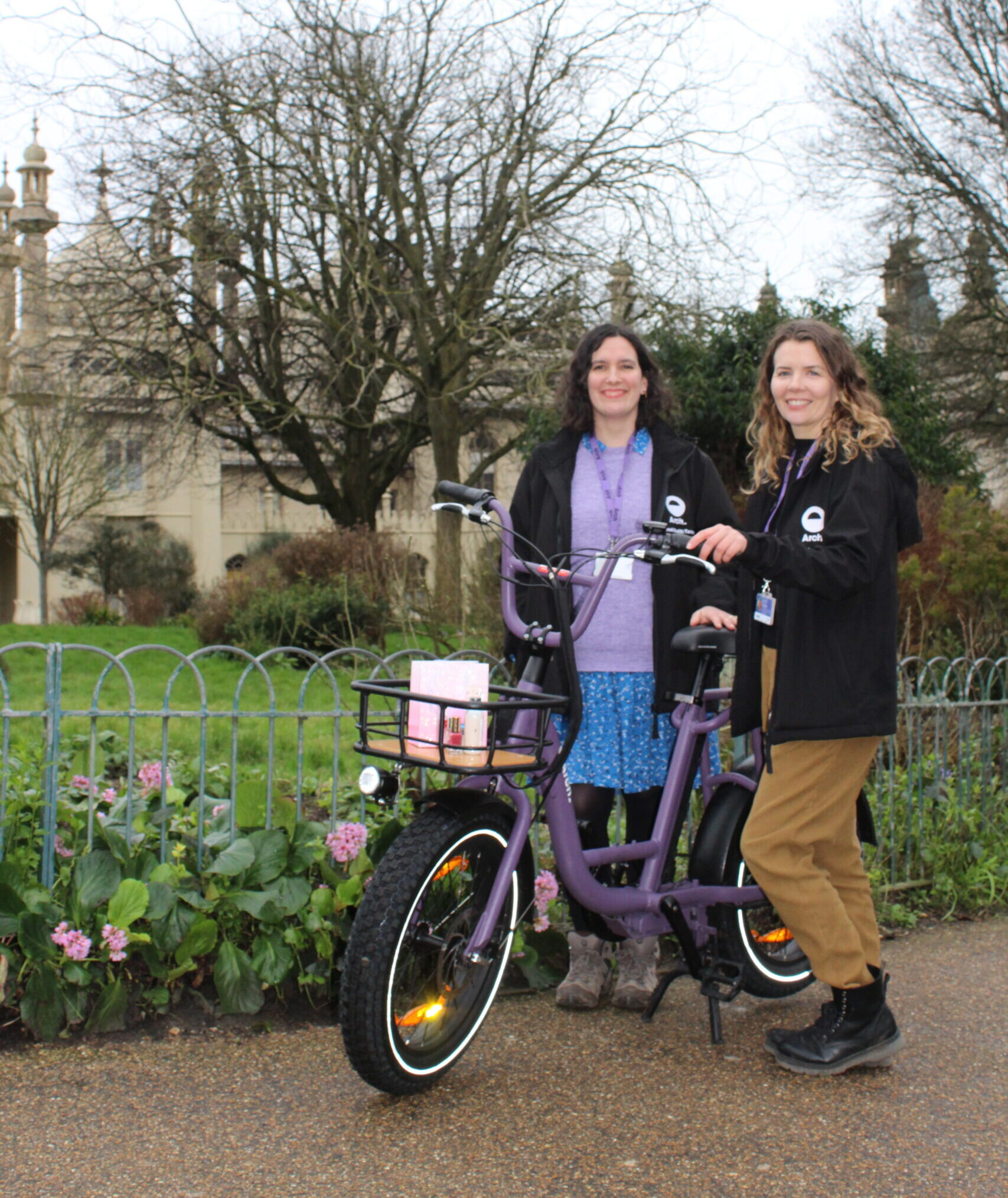 Two women standing in a park next to a bike, smiling at the camera
