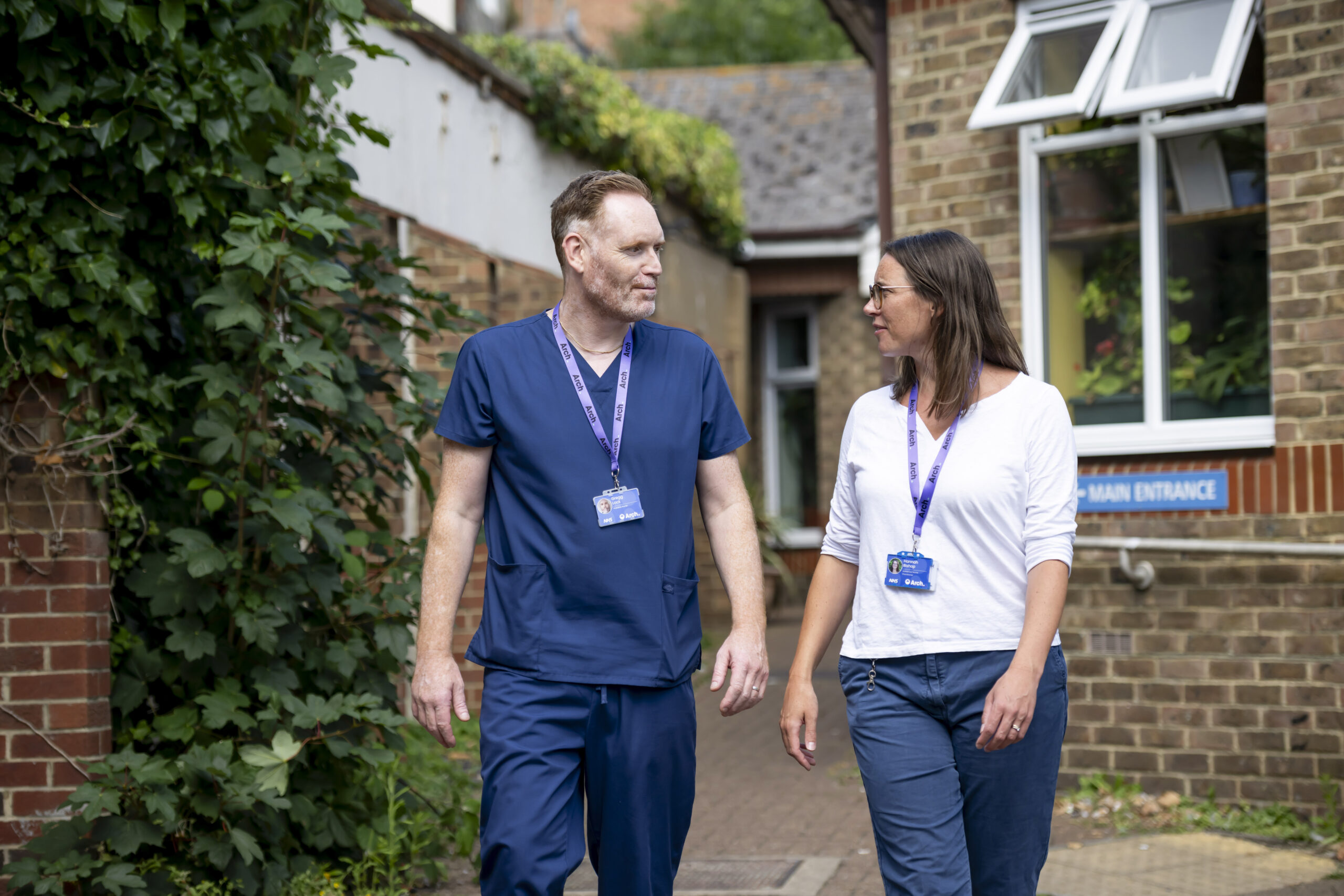 A female nurse and male nurse talk while walking along the path outside the New Steine Mews hostel where Arch Health's Step Down Beds service is located.