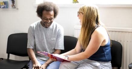 Arch patient and receptionist smiling while looking at a clipboard with a form together.