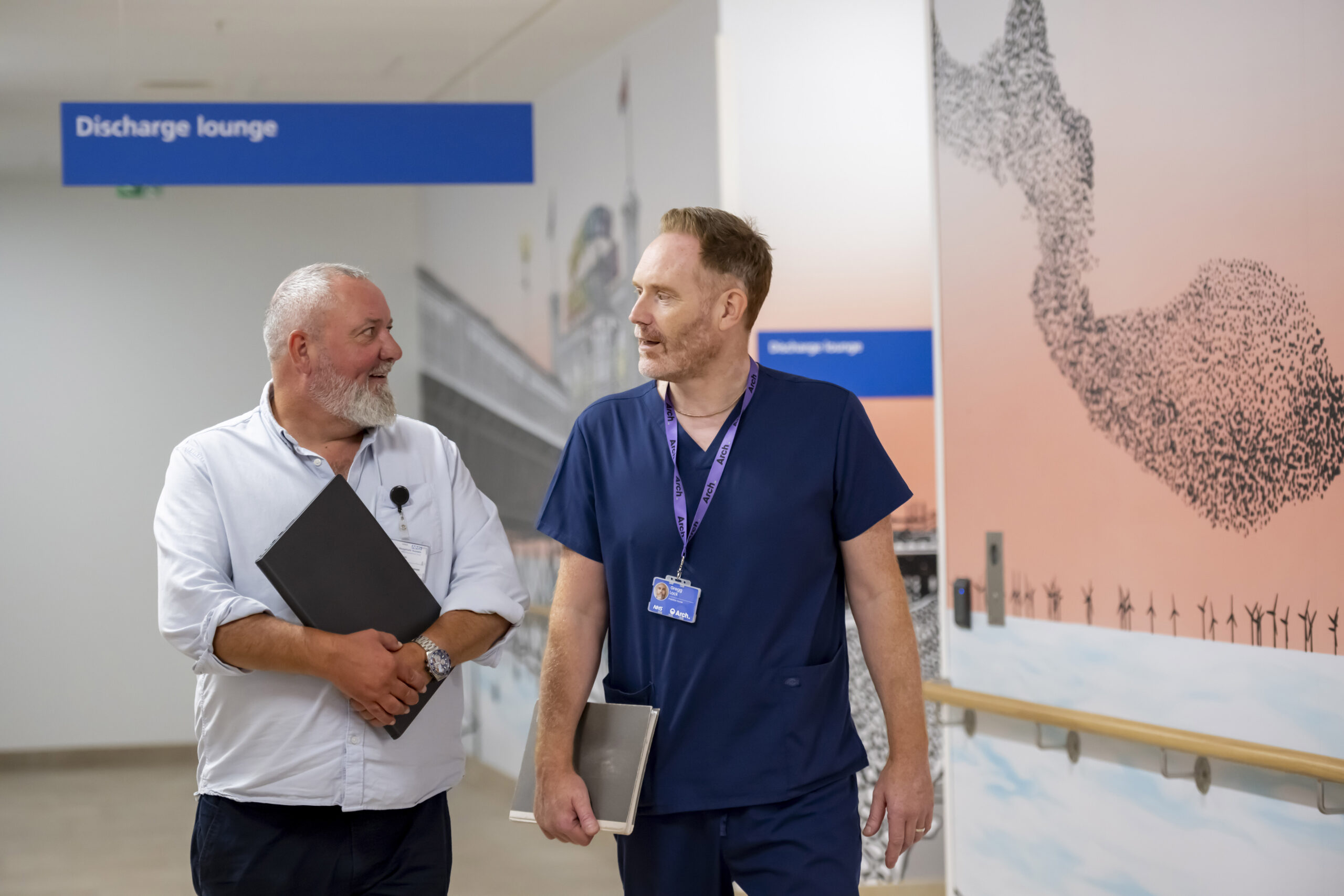 Two Pathway team members talk in the hospital corridor outside a sign saying Discharge Lounge