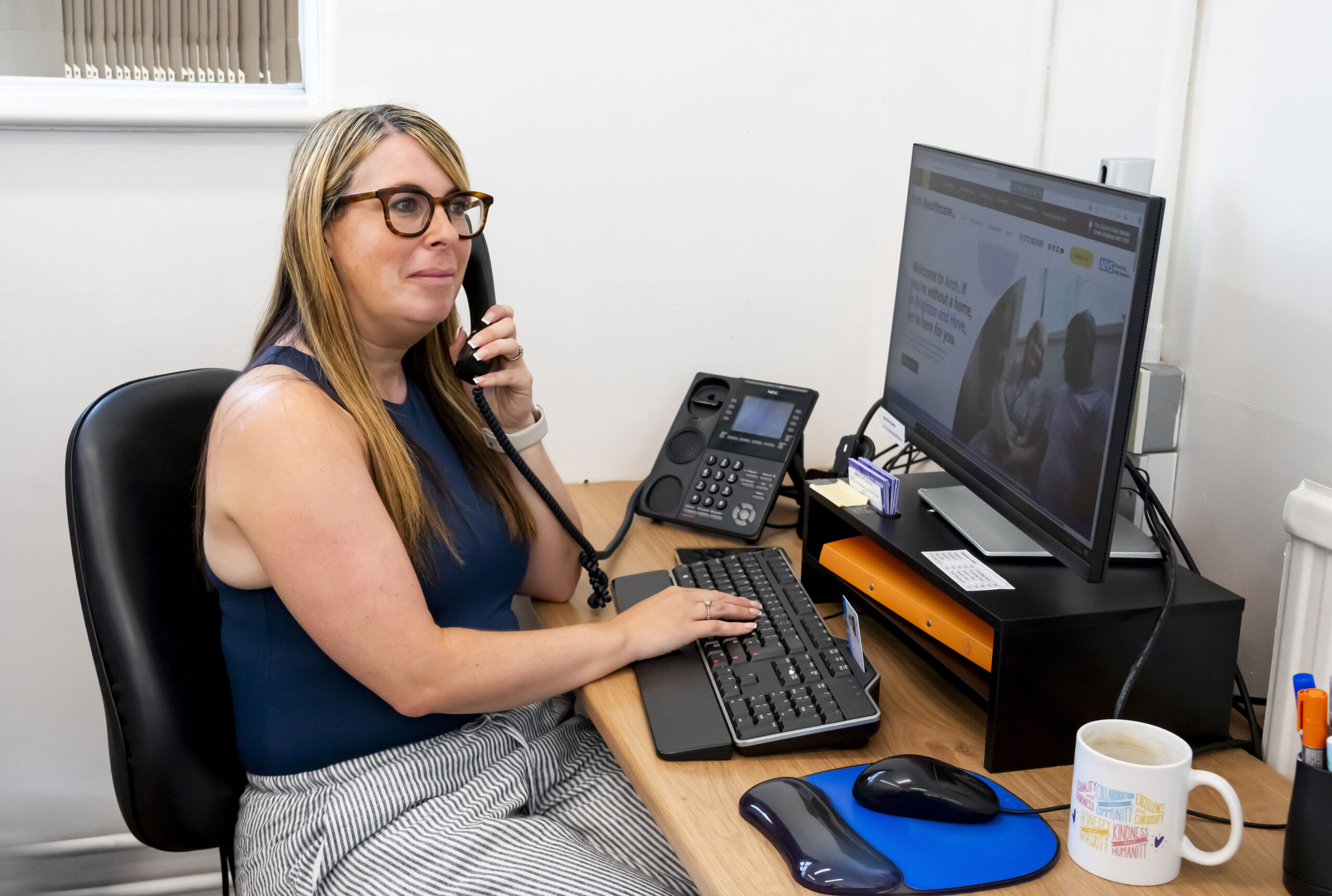 Arch receptionist talks on the phone while entering details onto a computer system.